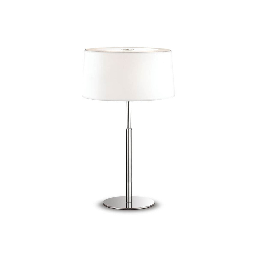 Lampe à poser blanche de face sur fond neutre, abat-jour cylindrique et pied chromé.