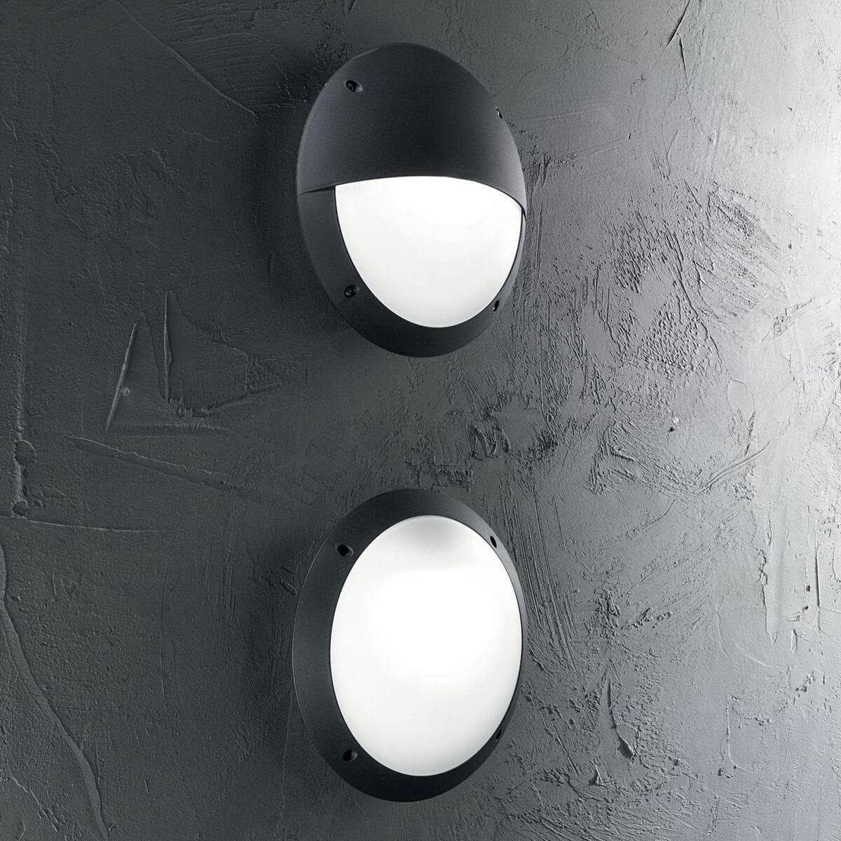 Deux appliques noires allumées sur un mur gris texturé en ambiance.