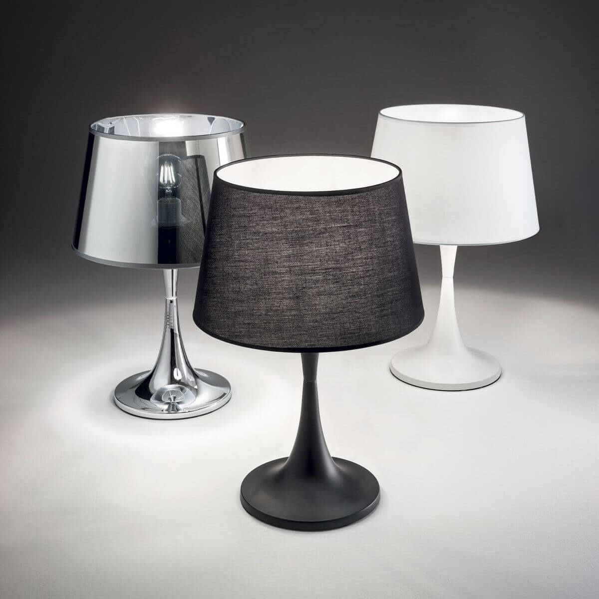 Trois lampes identiques en finitions noire, blanche et chromée, sur fond gris