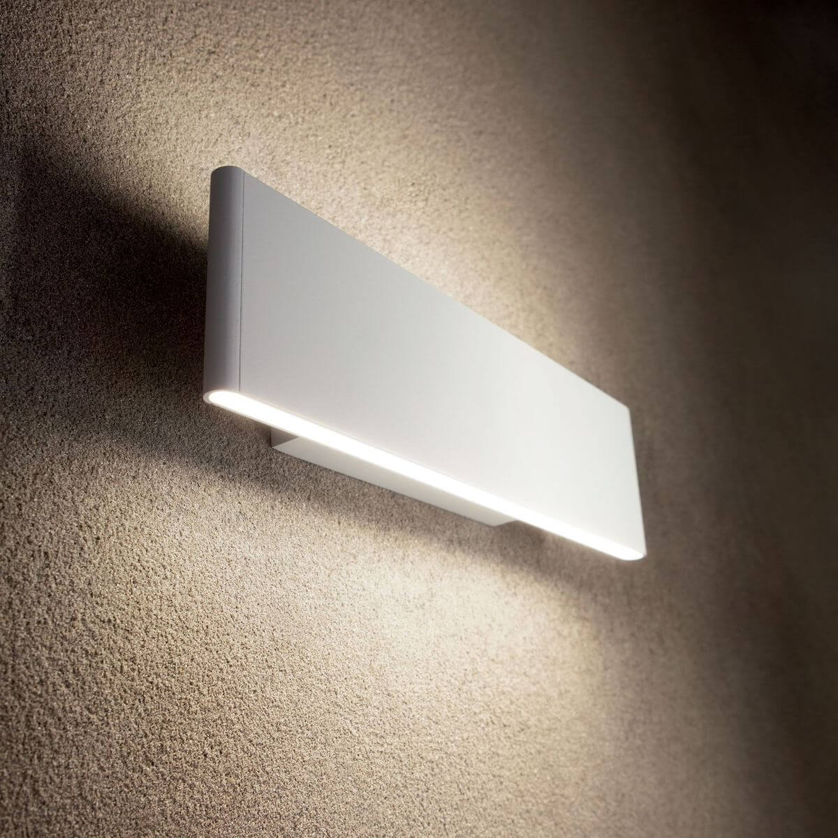 Luminaire mural blanc allumé, fixé sur un mur texturé beige clair