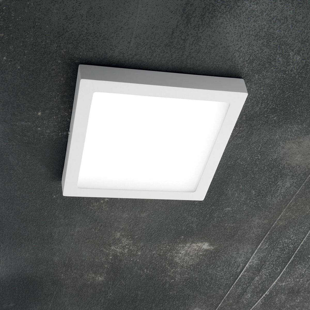 Plafonnier blanc carré installé sous un plafond sombre, vue en contre-plongée montrant le profil
