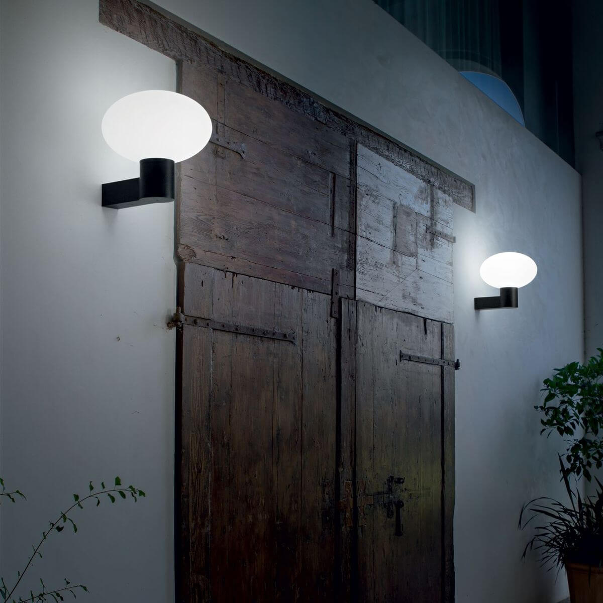 Mise en ambiance nocturne sur mur blanc, deux appliques éclairant une porte ancienne