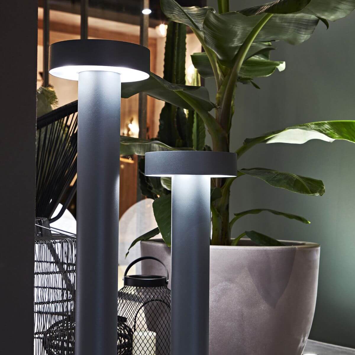 Mise en ambiance nocturne de deux bornes hautes parmi des plantes vertes en pot