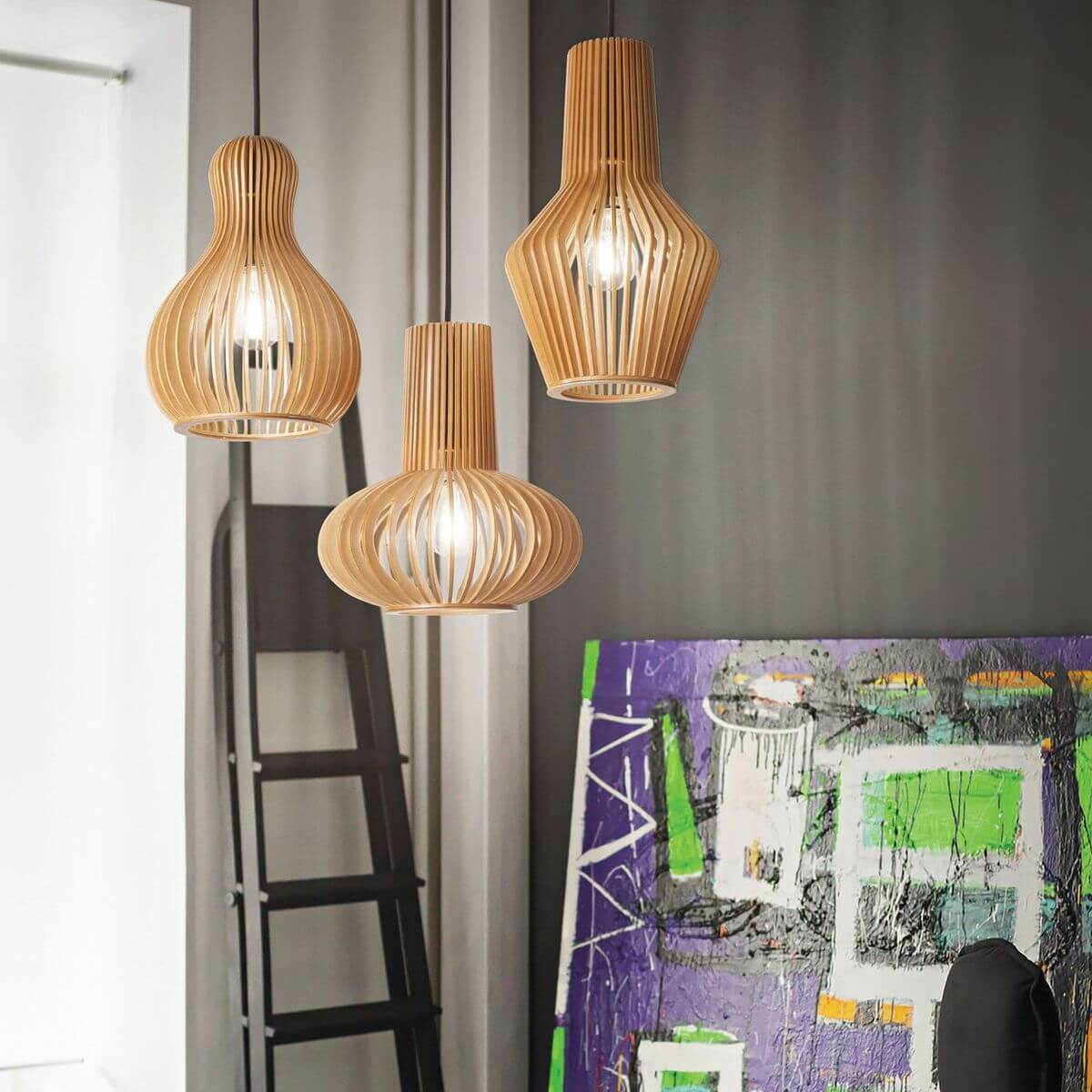 Trois suspensions en bois allumées en intérieur, devant une œuvre colorée et une échelle.