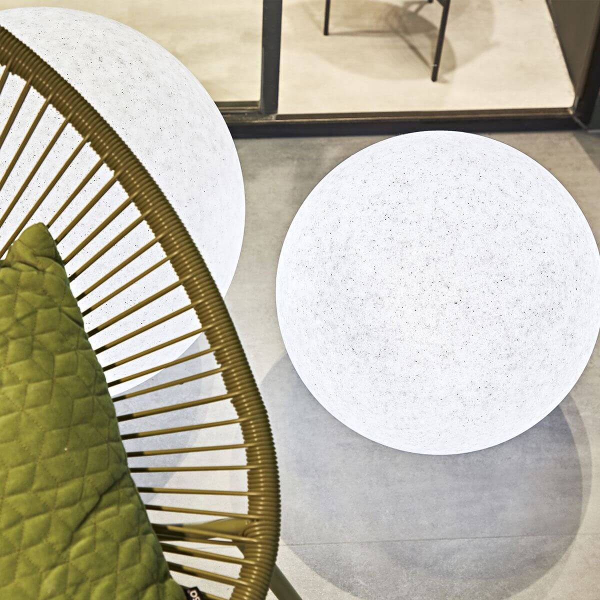 Deux globes lumineux blancs près d'un fauteuil en rotin et coussins verts