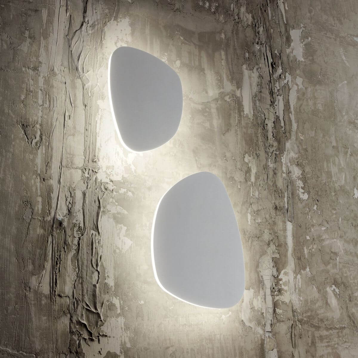 Mise en ambiance de deux appliques murales blanches allumées sur un mur en béton brut.
