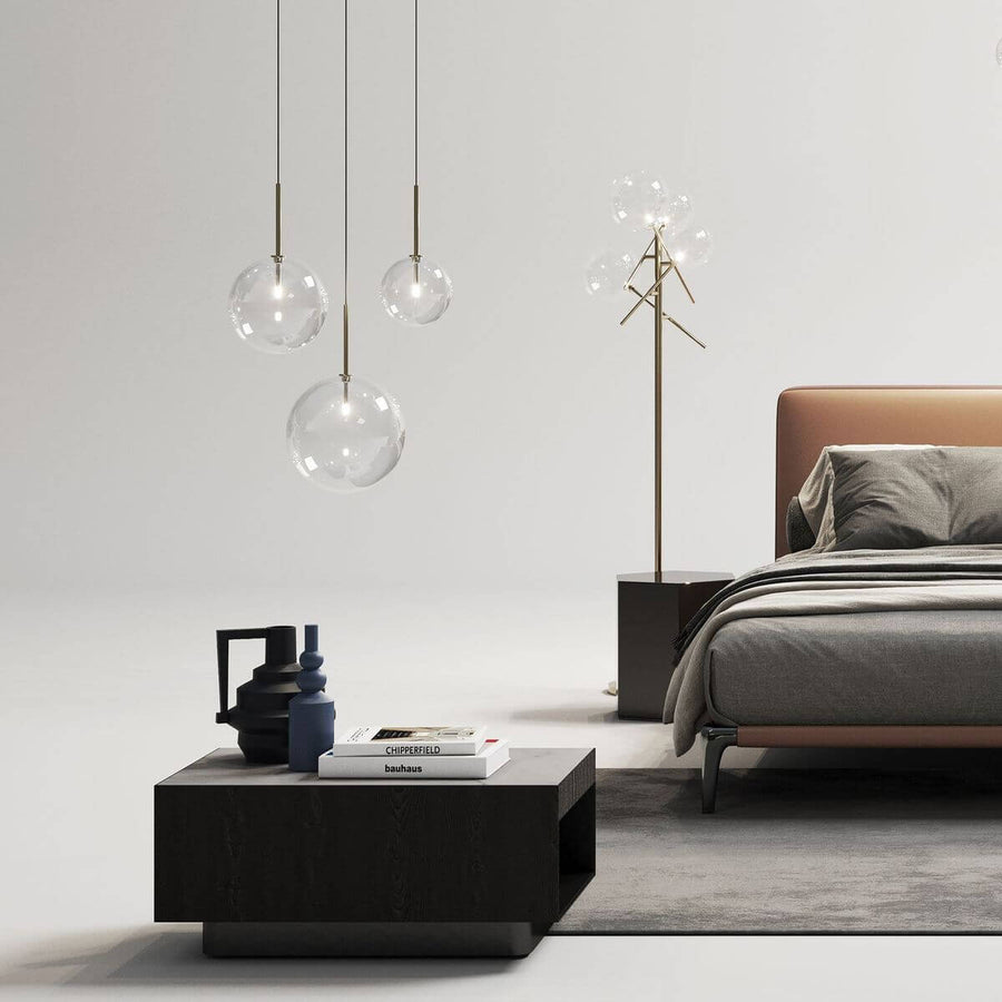 Suspensions en verre transparent éclairées dans une chambre contemporaine, avec lit, table basse et lampadaire