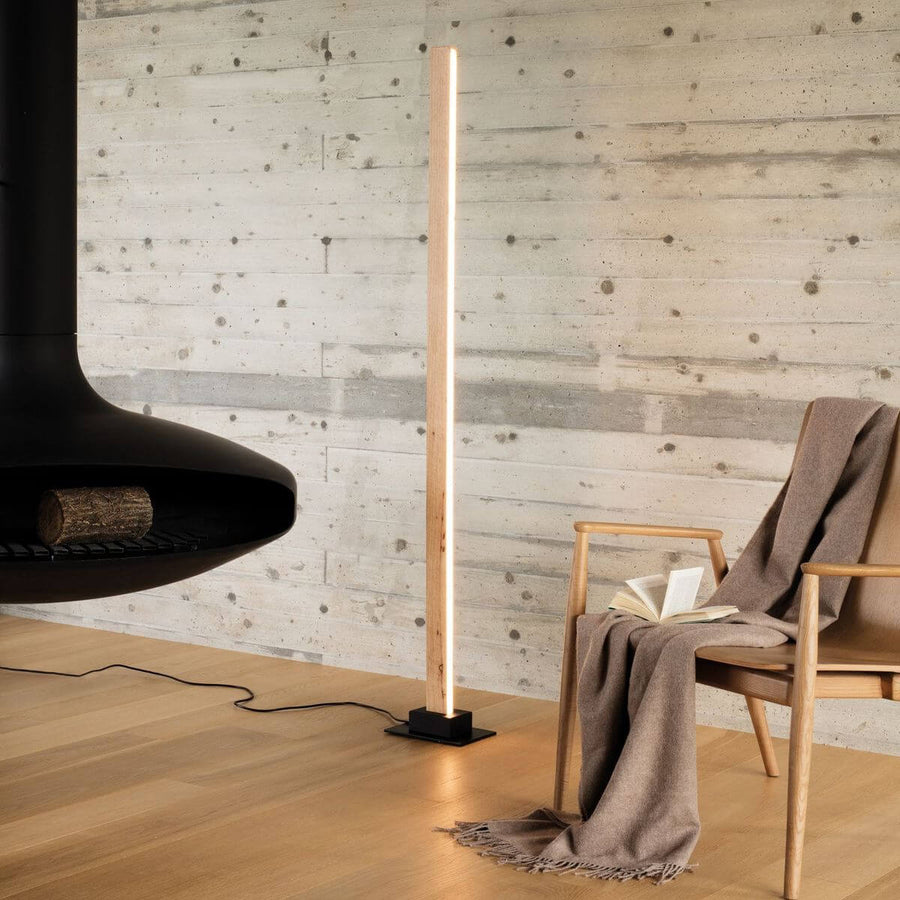 Lampadaire allumé dans un salon près d'une cheminée noire et d'un fauteuil en bois.