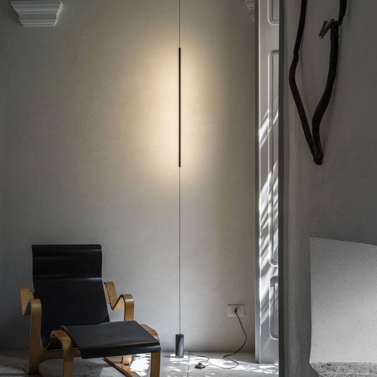 Mise en ambiance : lampe verticale éclairant un mur près d'un fauteuil noir