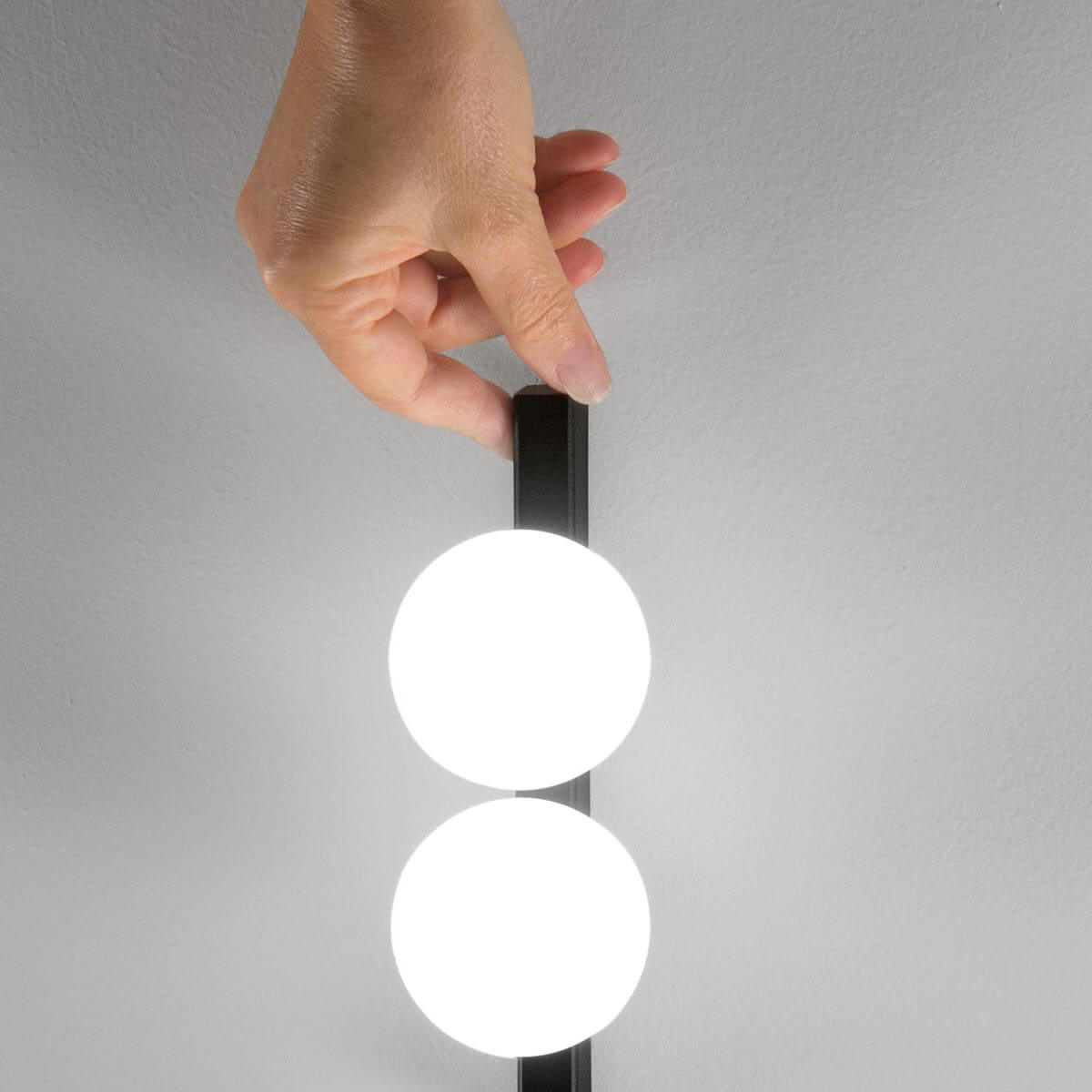 Main fixant le support noir de l applique au mur, vue rapprochée