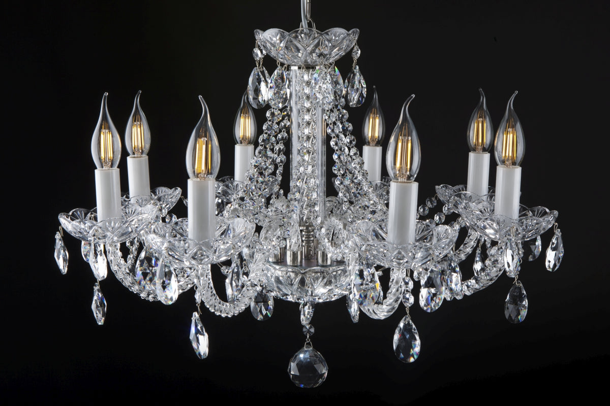 Vue de face du lustre suspendu, cristal transparent et ampoules allumées sur fond noir.