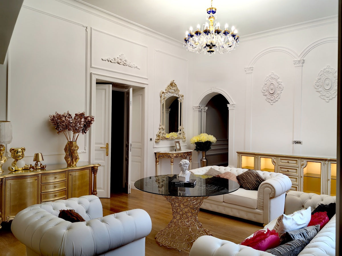 Mise en ambiance dans un salon classique blanc et doré, lustre suspendu au plafond.