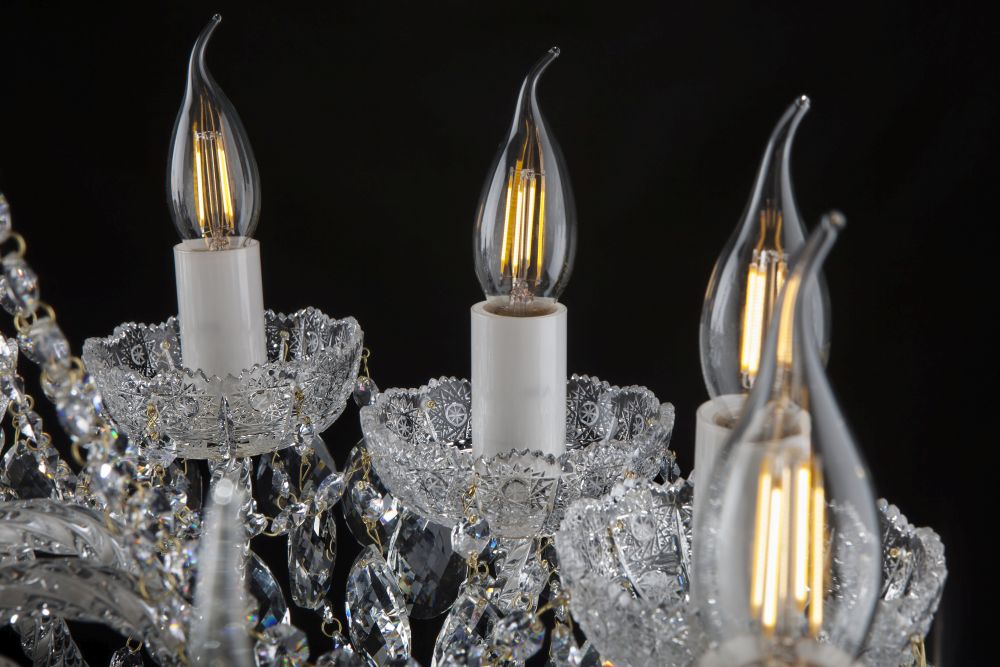 Gros plan sur trois ampoules flamme allumées, douilles blanches et coupelles en cristal ciselé