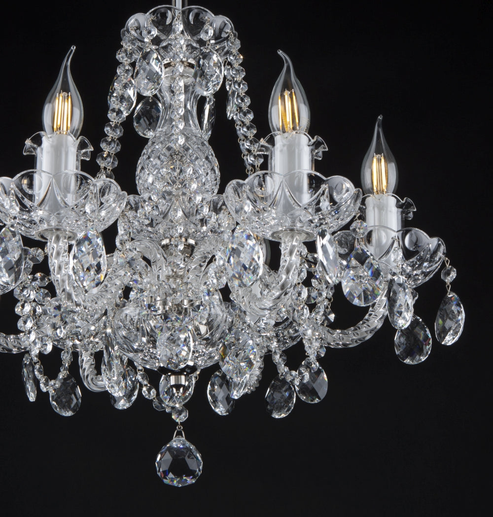 Vue rapprochée du lustre, cristaux taillés et ampoules allumées sur fond noir.