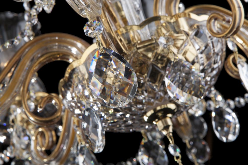 Zoom sur une pampille pendante facettée et les volutes dorées du luminaire