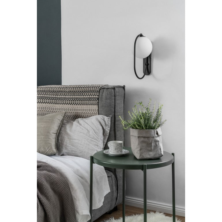 Ambiance chambre : applique noire éclairée au-dessus table de chevet verte