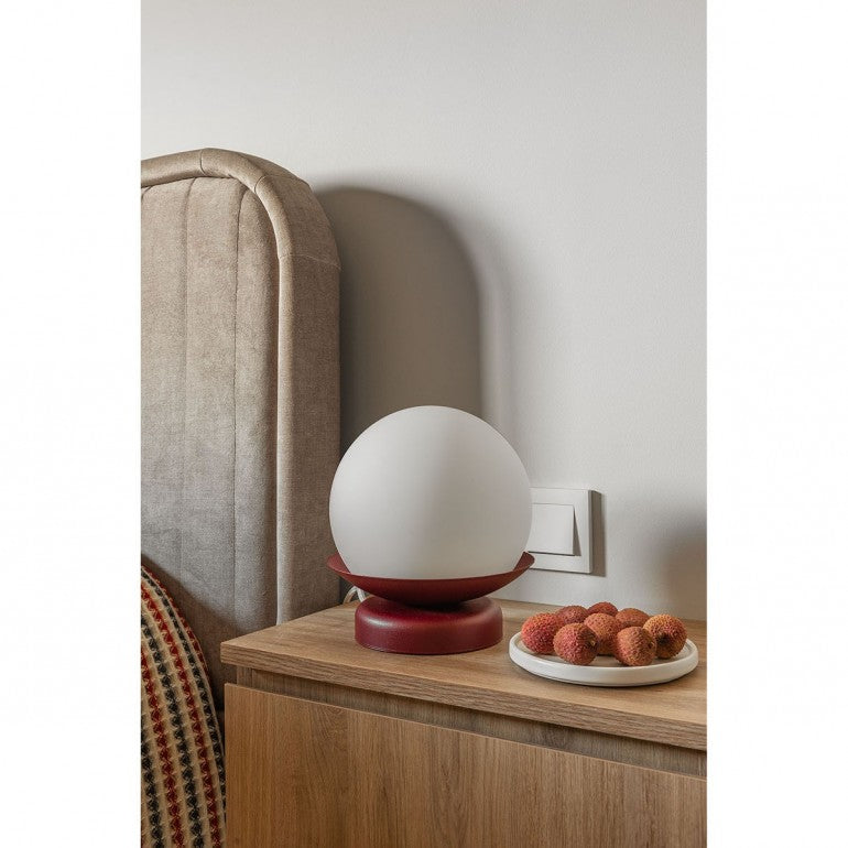 Lampe bordeaux posée sur une table de nuit en bois, tête de lit capitonnée