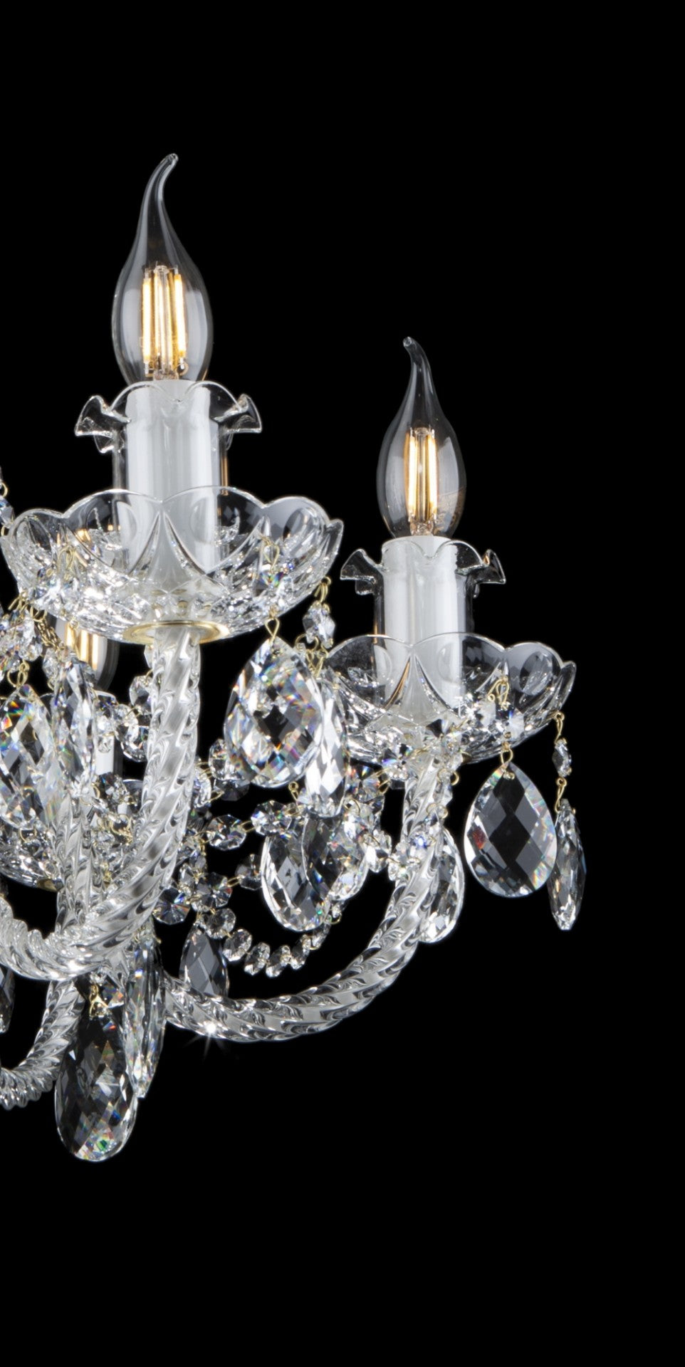 Gros plan sur les bras torsadés, les pendants octogonaux et les chaînettes dorées du lustre.