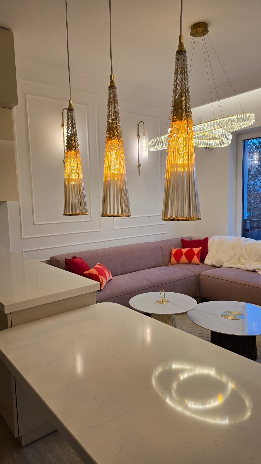 Mise en ambiance salon: suspensions allumées au-dessus d'un canapé rose et tables basses.
