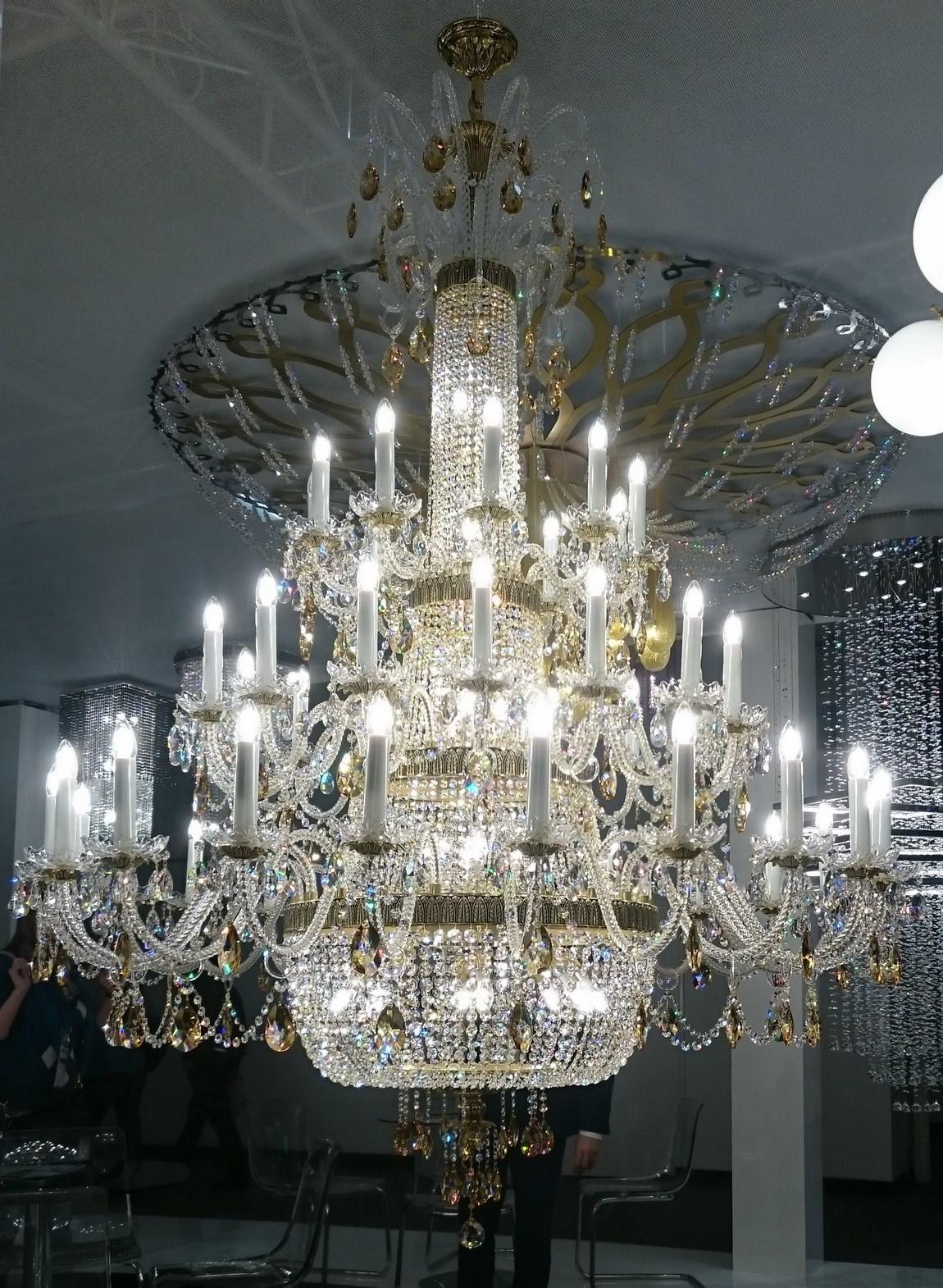 Lustre suspendu au plafond dans une salle d'exposition, avec des personnes autour.