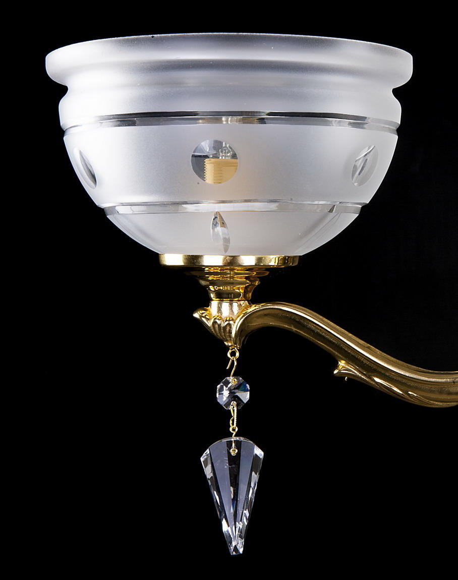 Gros plan sur une coupelle en verre dépoli et pampille en cristal du luminaire doré.