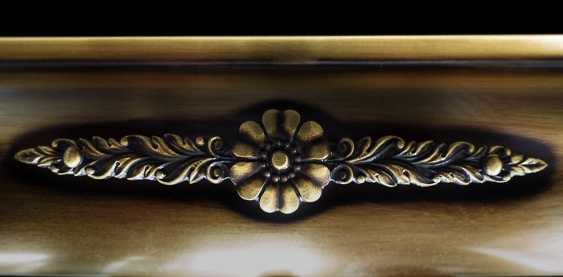 Gros plan du médaillon floral ciselé et des feuillages patinés sur le cylindre