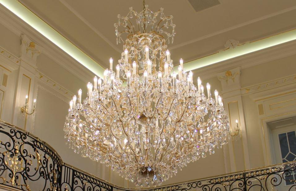 Vue rapprochée du lustre sous un plafond mouluré, étages de cristaux et bras allumés.