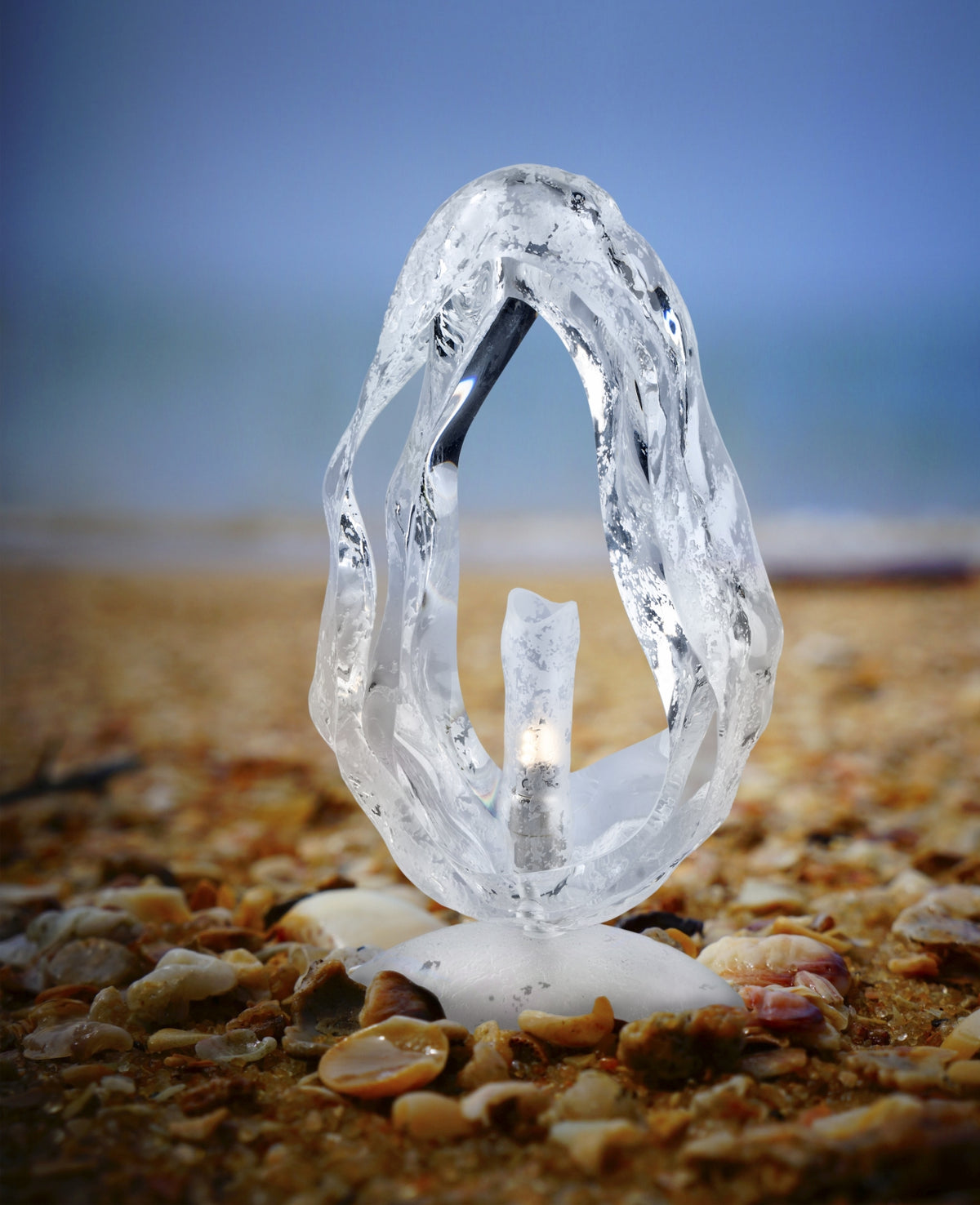 Mise en ambiance sur une plage de galets, lampe posée sur le sable.