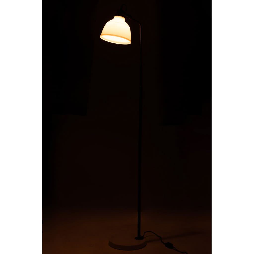 Lampadaire allumé dans une pièce sombre, lumière chaude diffusée par l'abat-jour blanc.