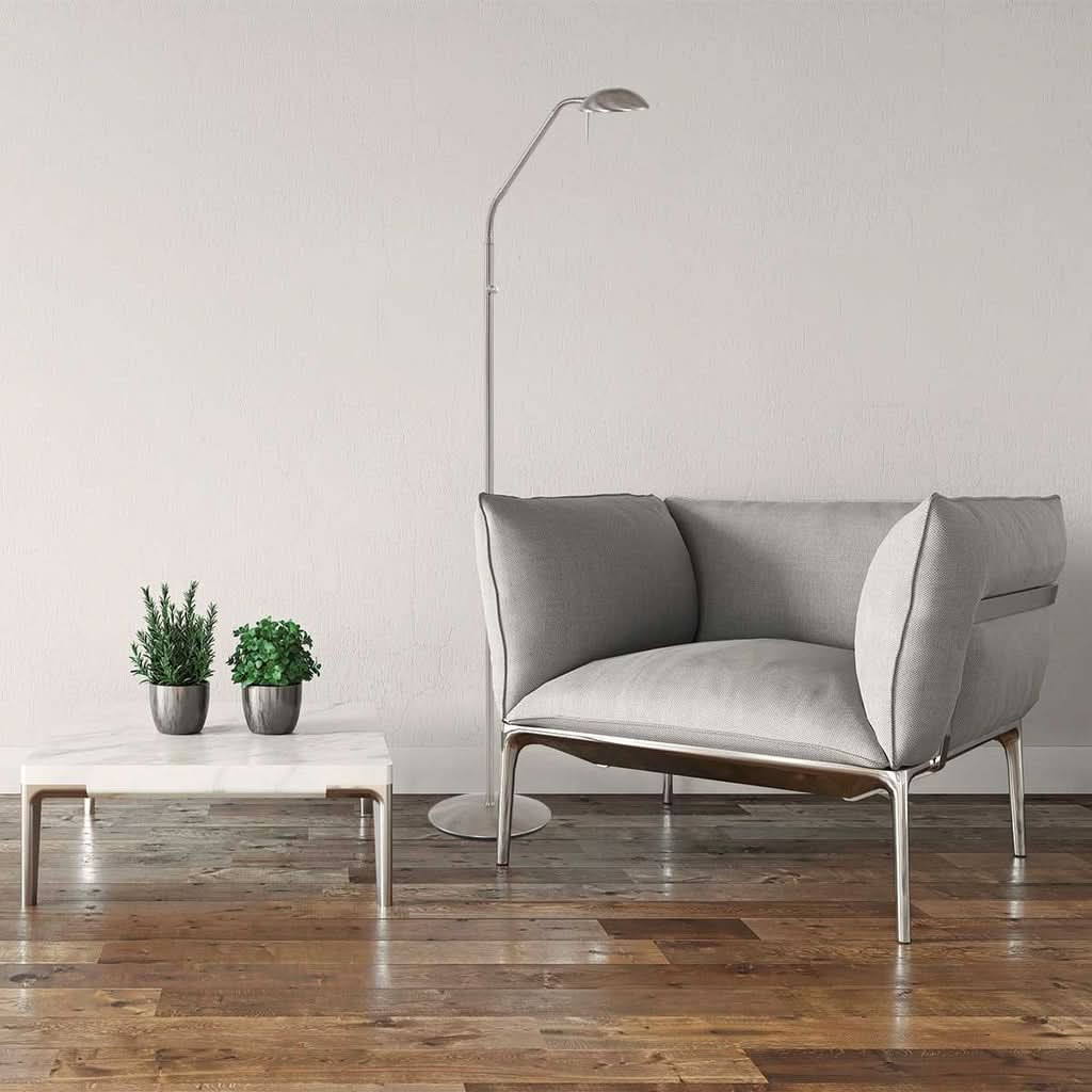 Lampadaire fin en acier derrière un canapé gris, table basse en marbre et plantes.