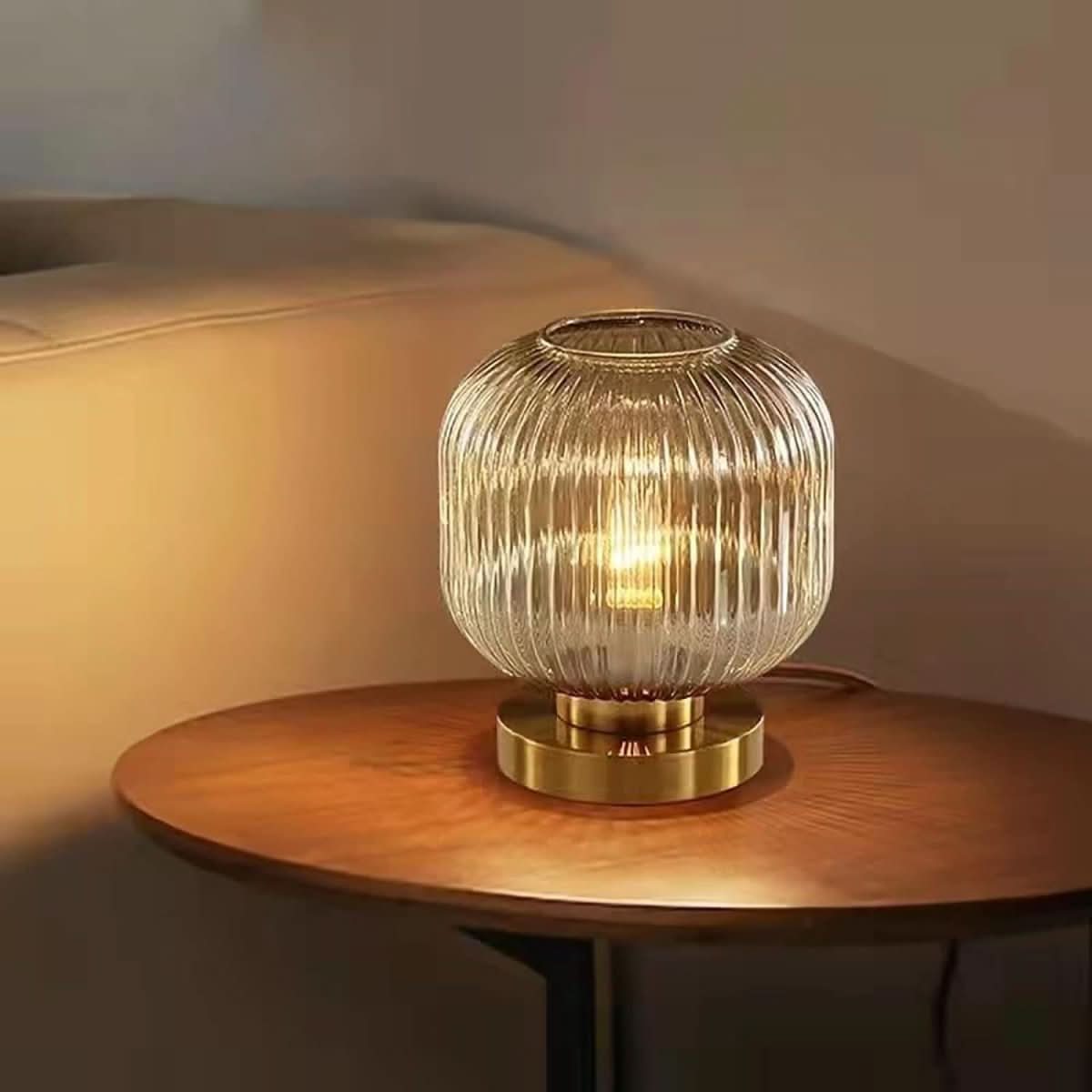 Lampe en verre transparent cannelé allumée, posée sur table basse ronde en bois