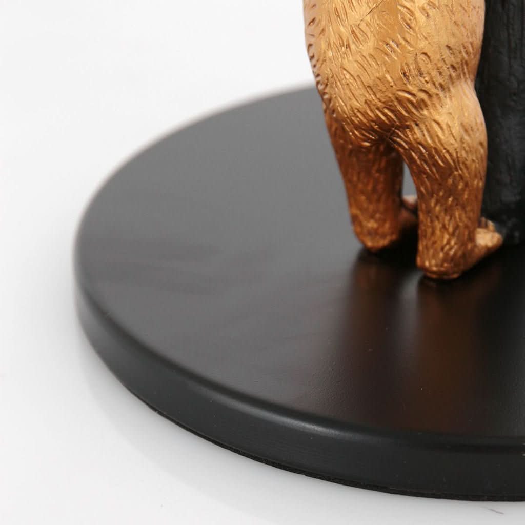 Détail de la base ronde noire et des pattes arrière dorées de l'ours.