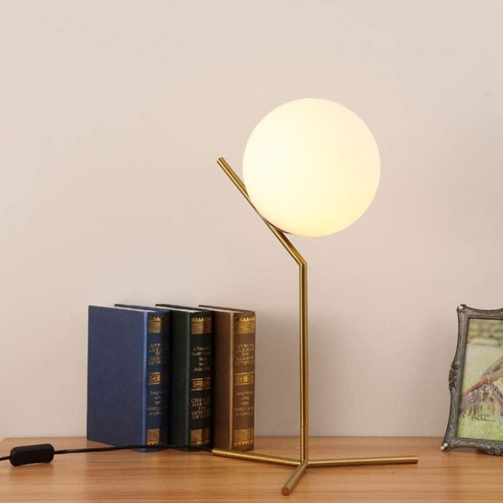 Lampe boule sur pied avec livres reliés et cadre photo sur une commode claire.