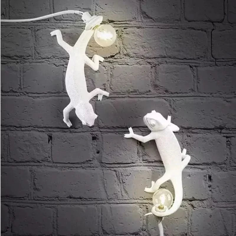 Deux caméléons blancs accrochés à un mur de briques grises, éclairés.