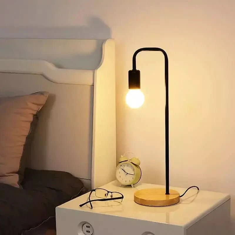 Lampe allumée sur table de nuit blanche près d'un lit, réveil et lunettes posés à côté