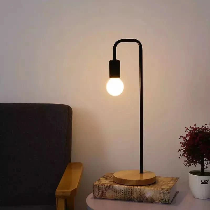 Lampe noire posée sur un livre, devant un fauteuil et une petite plante en pot
