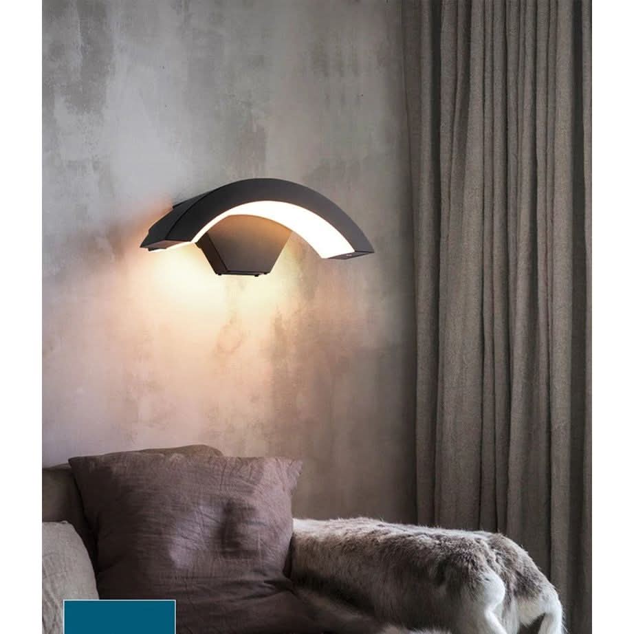 Applique murale cintrée noire diffusant une lumière chaude au-dessus d'un canapé en tissu