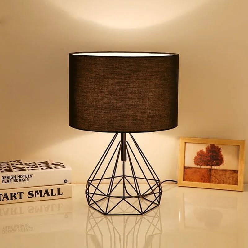 Lampe noire à abat-jour sombre allumée, posée devant des livres et un cadre photo.
