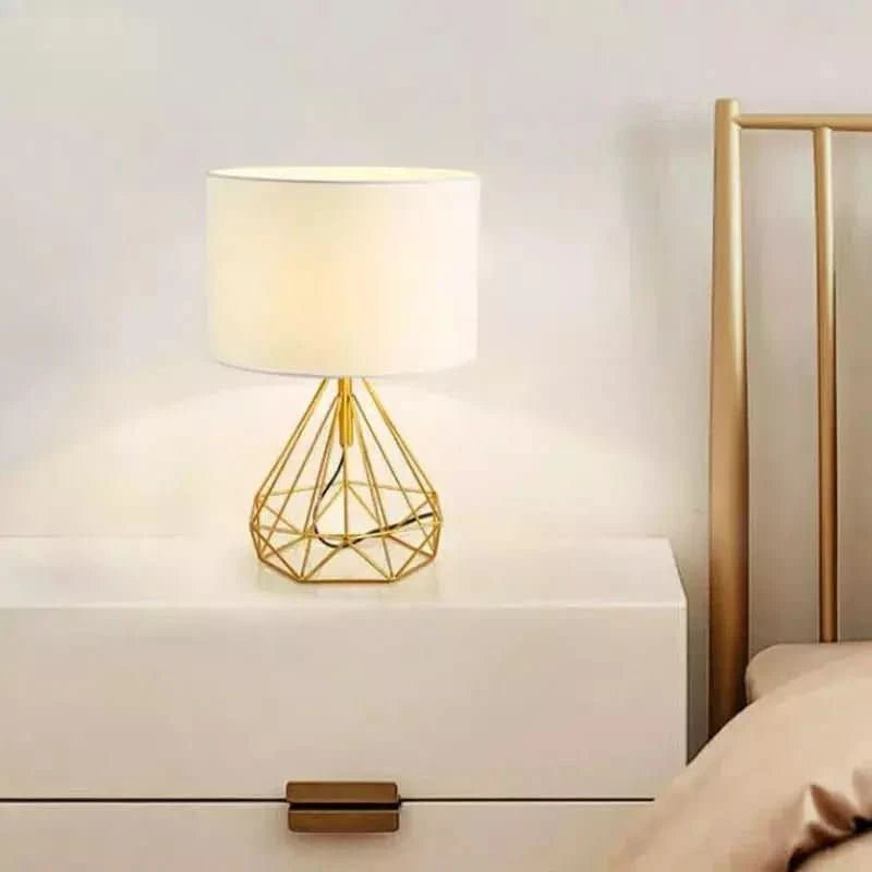 Version dorée de la lampe sur une table de chevet blanche, près d'un lit.
