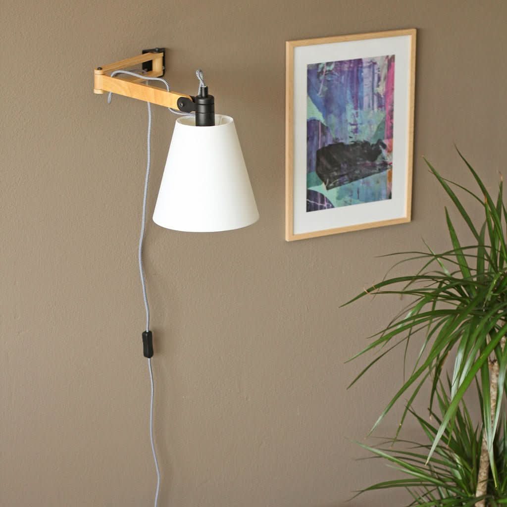 Lampe fixée au mur beige, câble tombant près d'un cadre et plante