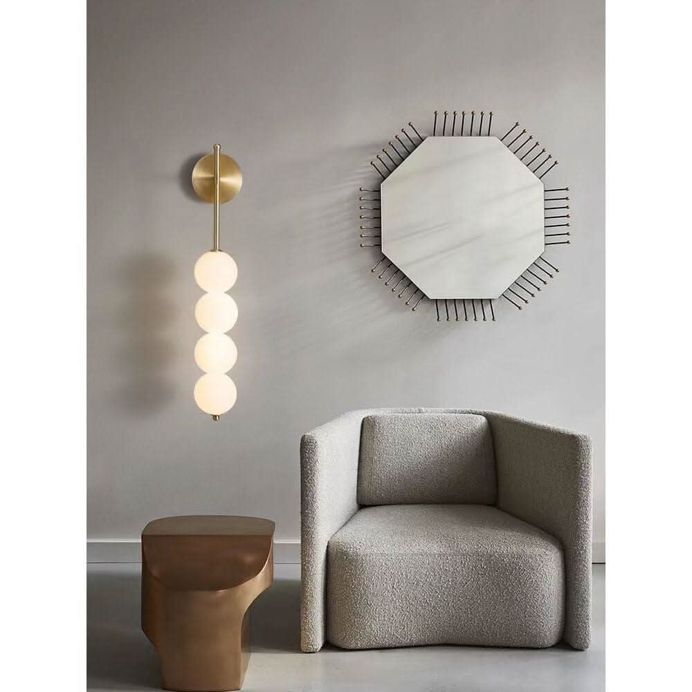 Mise en ambiance salon, applique laiton devant un miroir octogonal et un fauteuil