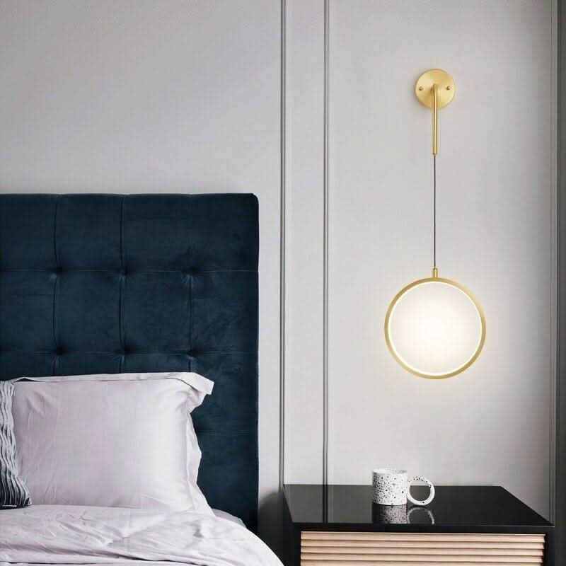 Lampe murale laiton allumée devant tête de lit en velours bleu nuit.