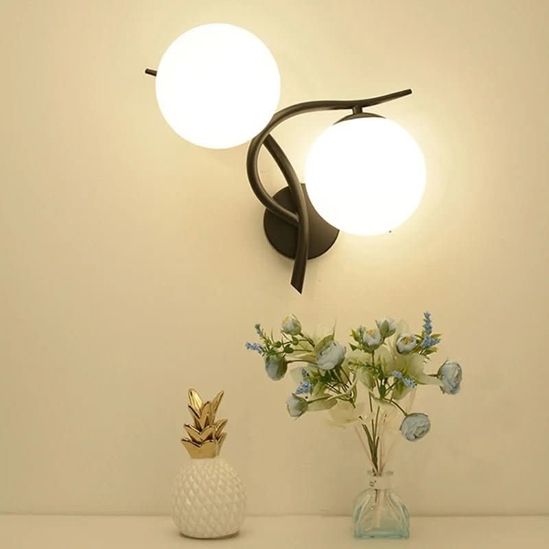 Luminaire mural allumé sur fond beige clair, avec vase de fleurs et objet décoratif