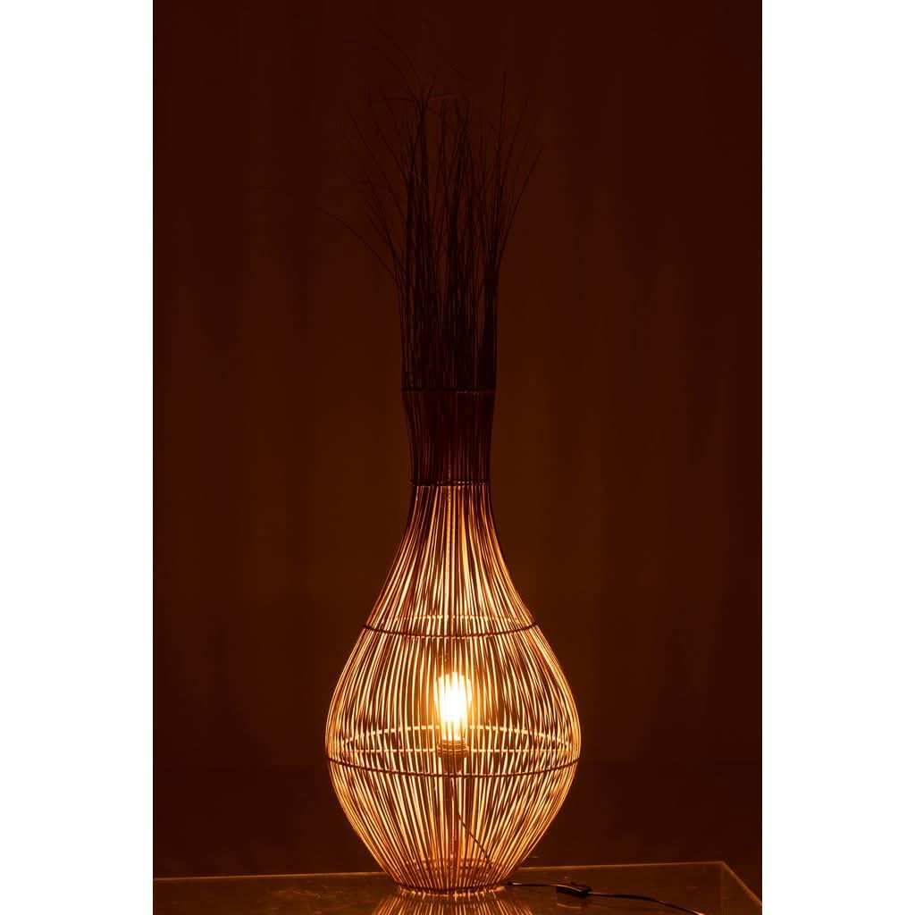 Lampe allumée dans pièce sombre, lumière chaude filtrant à travers tiges, ambiance cocooning.
