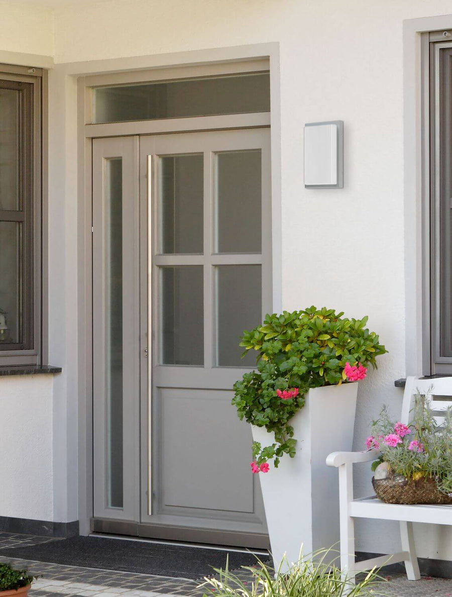 Applique extérieure grise fixée sur un mur blanc près d'une porte