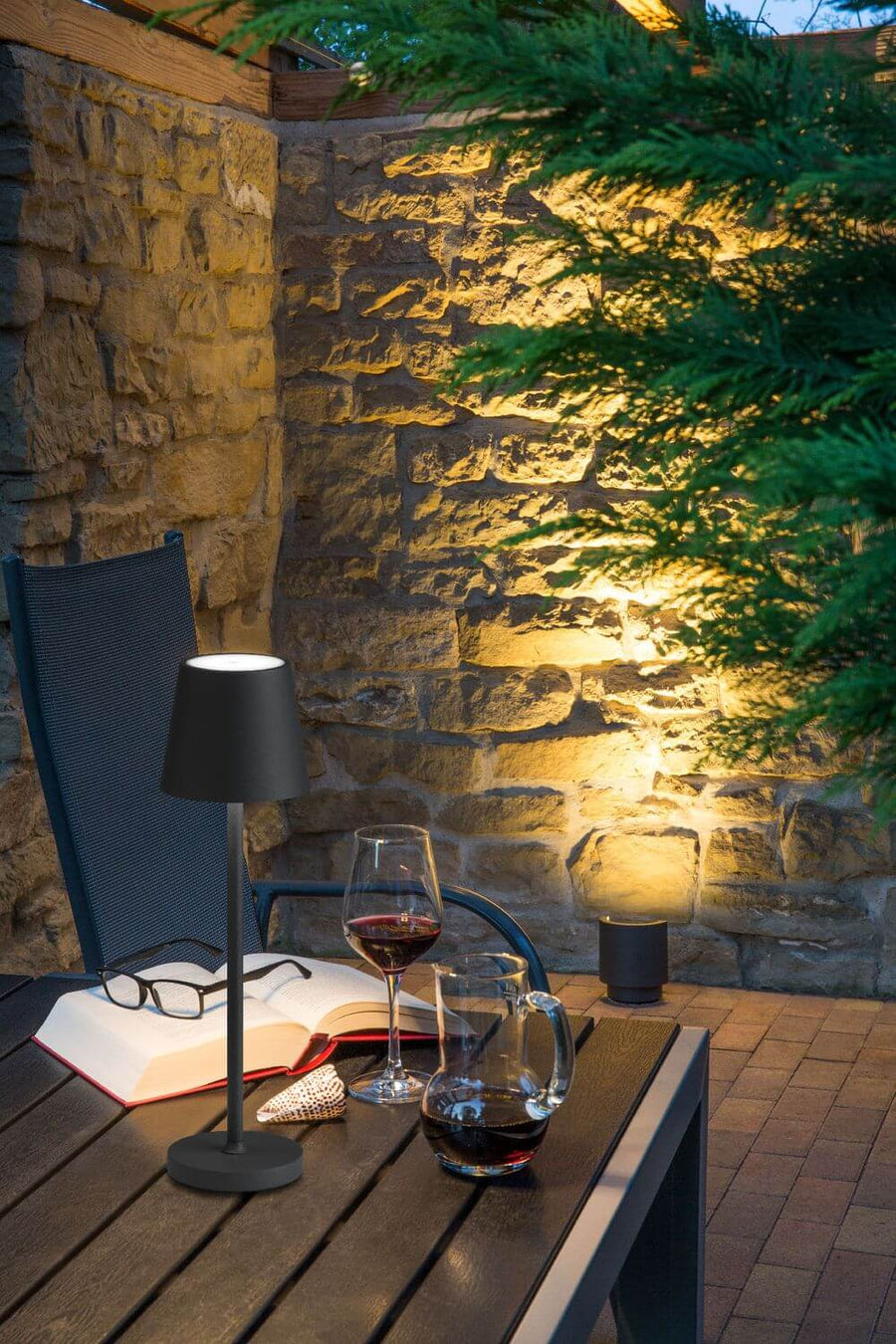 Scène rapprochée de terrasse éclairée, table en bois, lampe nomade et lecteur