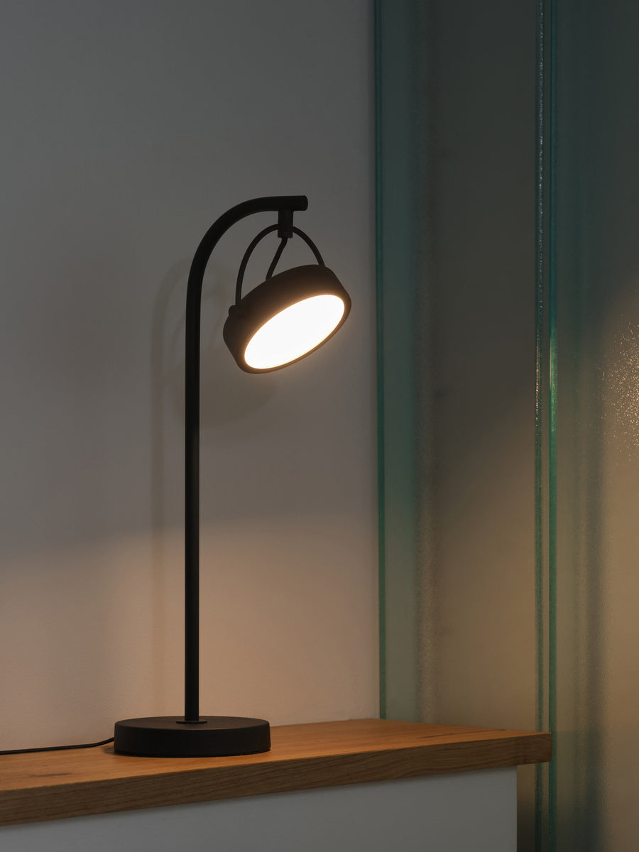 Lampe allumée sur une étagère en bois, halo chaud contre mur sombre.