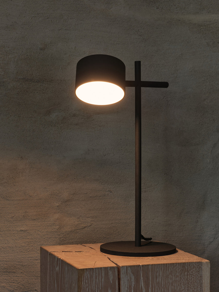 Lampe allumée posée sur un bloc de bois, halo lumineux sur mur gris.
