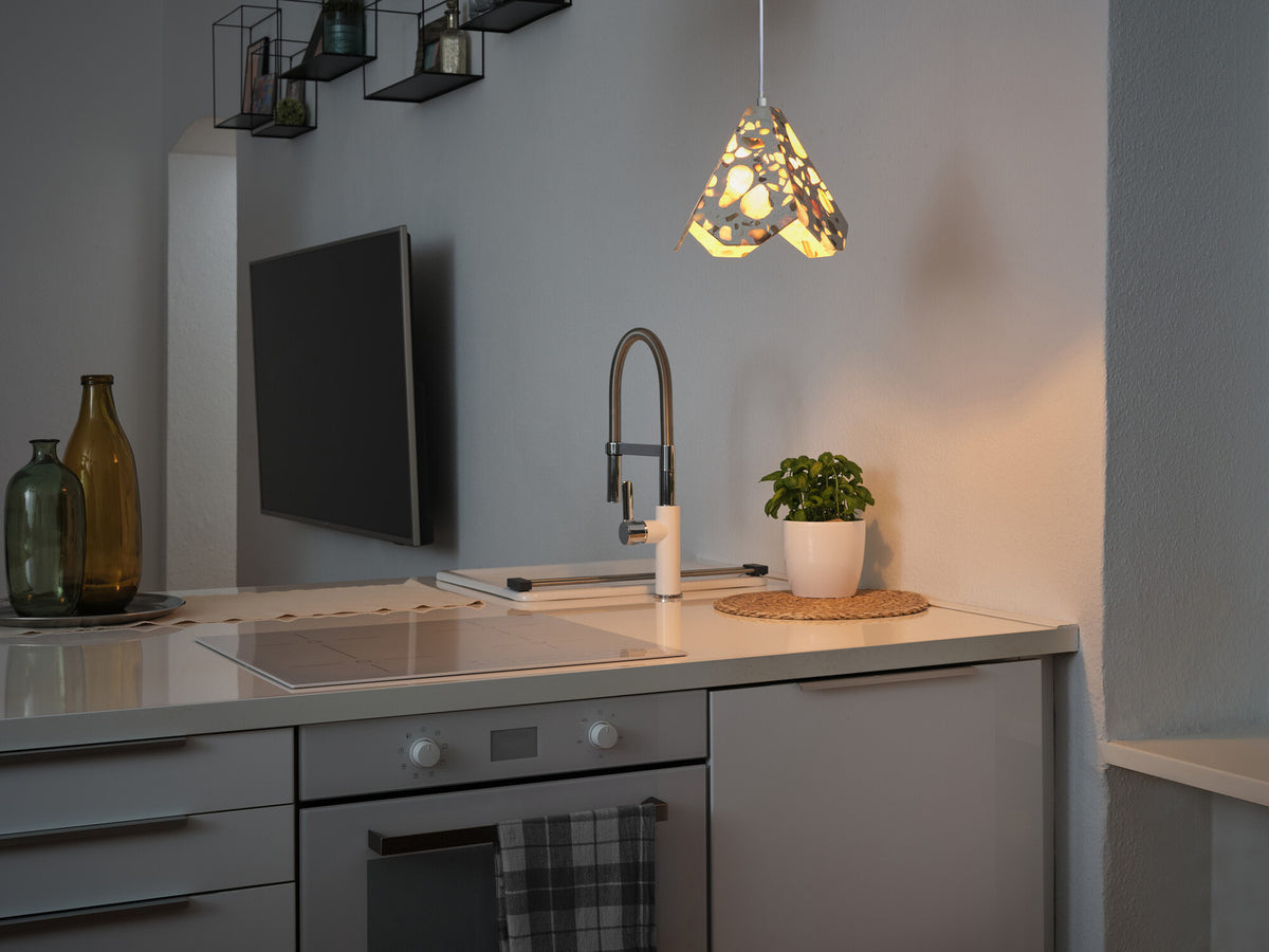 Suspension allumée au-dessus d’un plan de travail de cuisine gris, ambiance domestique.