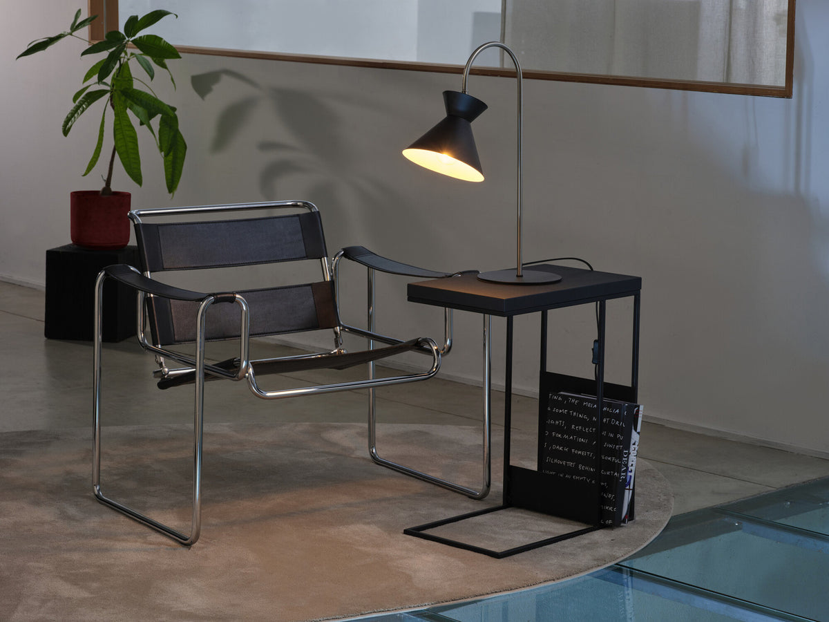 Mise en ambiance de la lampe allumée sur une table près d'un fauteuil design.
